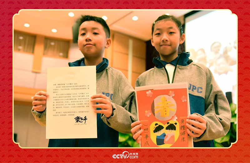 图为香港“少年警讯”成员郭宏晞（左）展示习主席回信、罗颢凝（右）展示送给习主席的贺卡并合影。